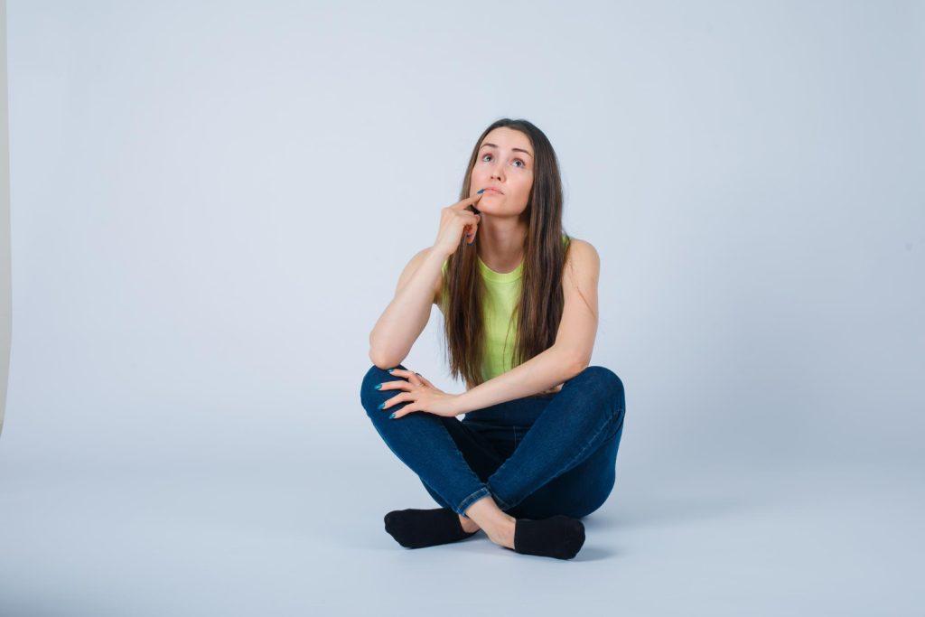 young-girl-is-sitting-floor-thinking-by-holding-forefinger-chin-white-background woman thinking